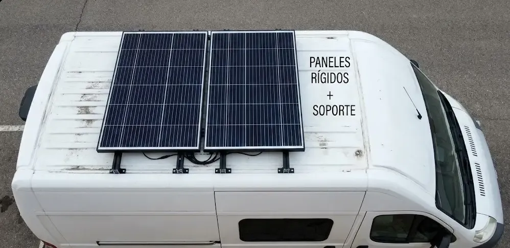 Fotografía aérea (vista cenital) de una furgoneta blanca. Se muestran dos paneles solares rígidos montados sobre el techo utilizando soportes negros elevados, dejando ver claramente el espacio de separación para la circulación del aire.