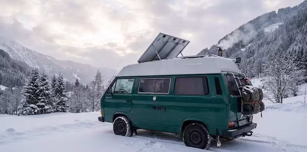 Furgoneta camper en la nieve con paneles solares inclinados captando luz difusa