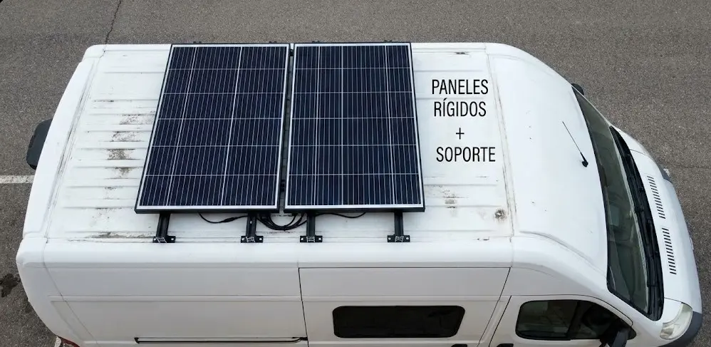 Fotografía aérea (vista cenital) de una furgoneta blanca. Se muestran dos paneles solares rígidos montados sobre el techo utilizando soportes negros elevados, dejando ver claramente el espacio de separación para la circulación del aire.